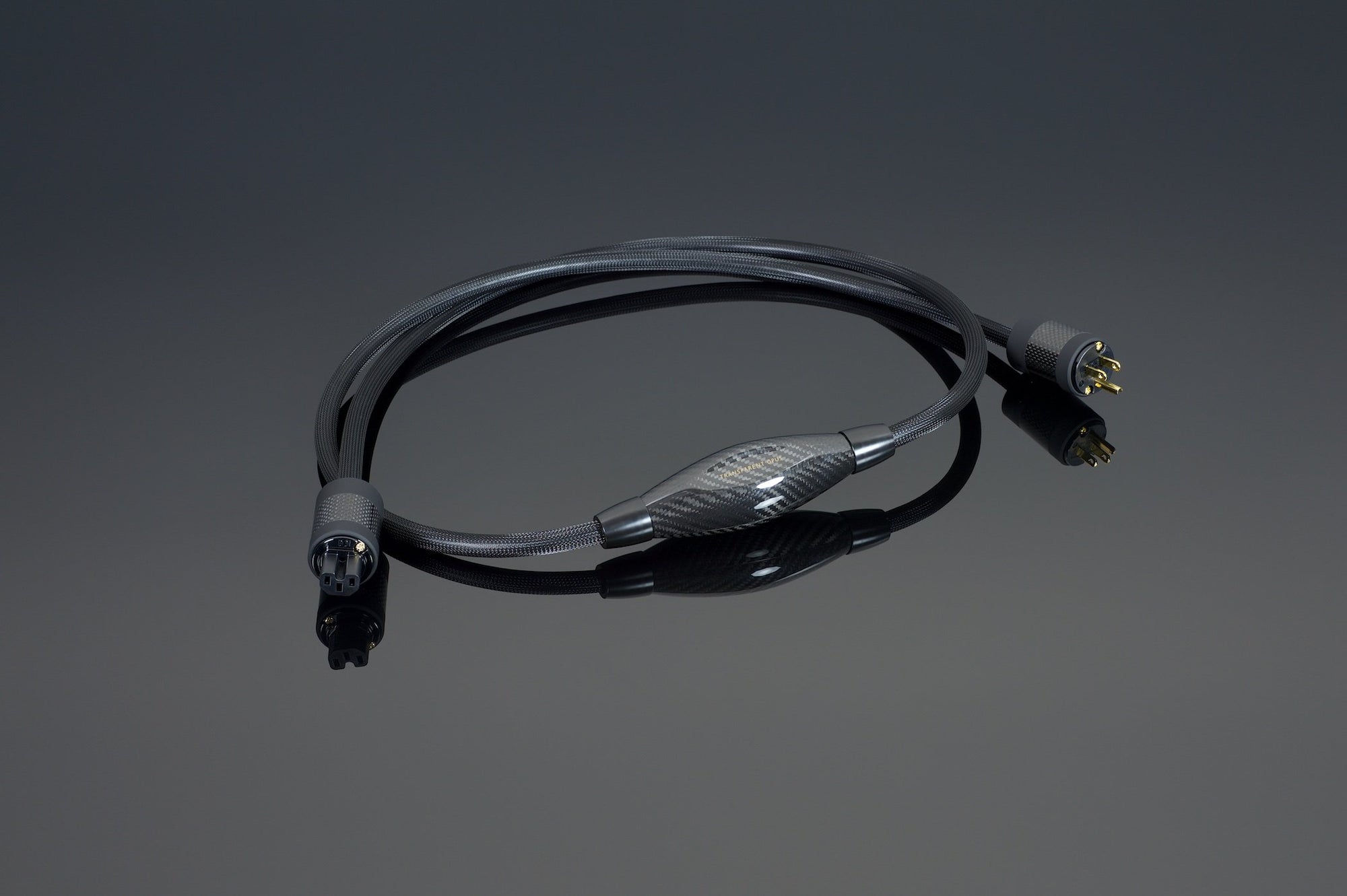 The OPUS Power Cord Source by Transparent Audio, a black cable featuring male and female XLR connectors, lies on a dark reflective surface, showcasing its OFHC power cable technology for optimal performance.